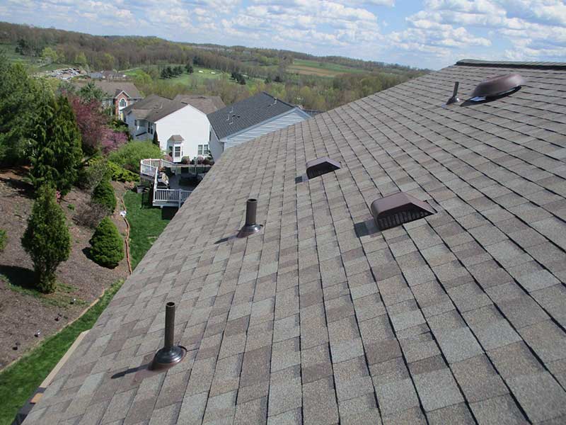 Top view of a residential roof looking out onto a suburb landscape with brand new gray asphalt shingles installed