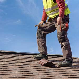 Worker on a light brown shingle roof inspecting it