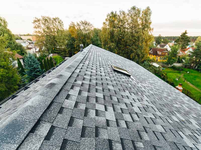 Top view of a residential roof with gray shingles overlooking a suburb landscape